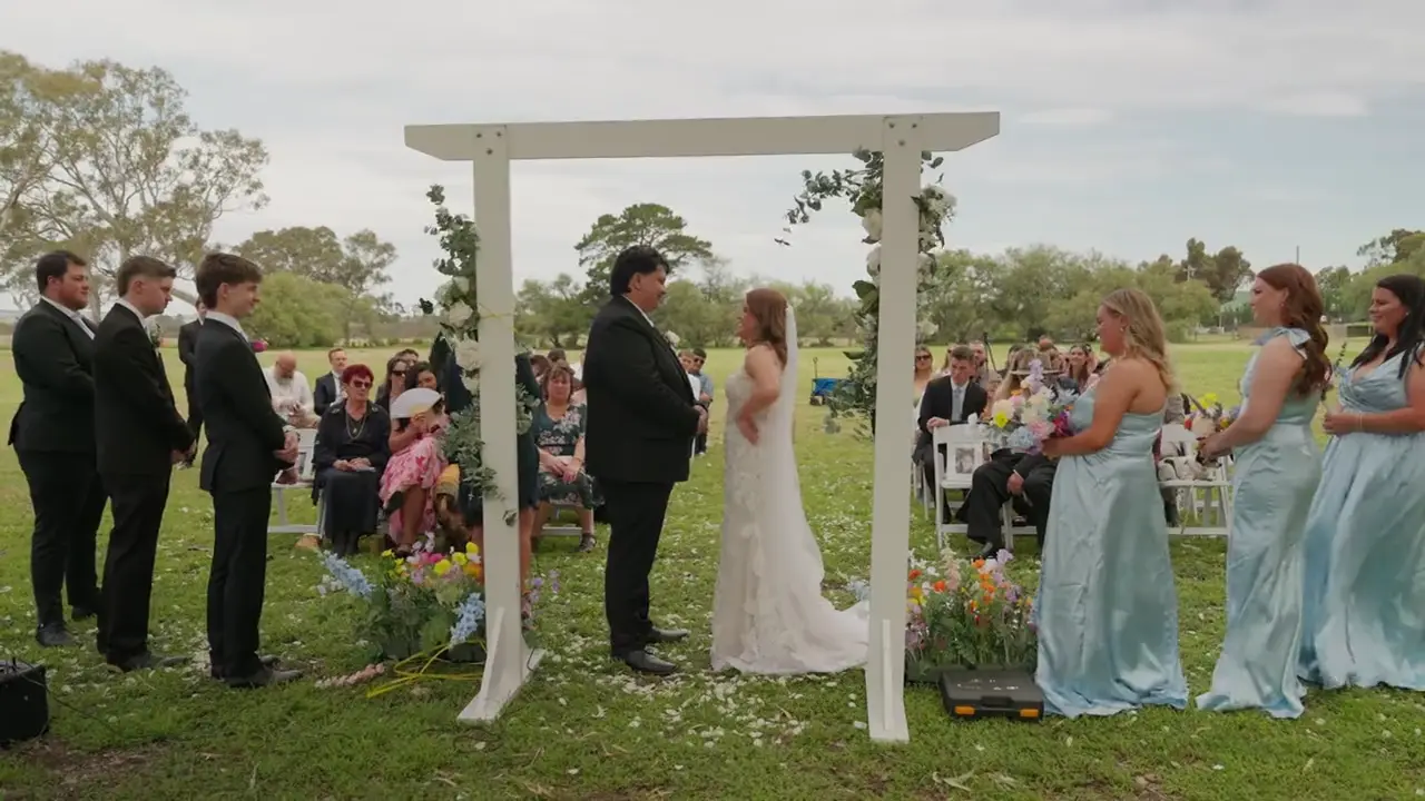 Isabel and Jack kissing beneath the arbour before walking back up the aisle through falling petals